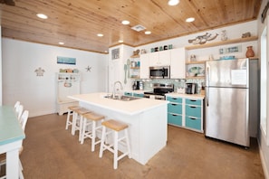 A kitchen with a central island, white cabinets, blue drawers, and a stainless steel refrigerator. - Another Day in Paradise - Beach Gear Credit Included! (Port Aransas)