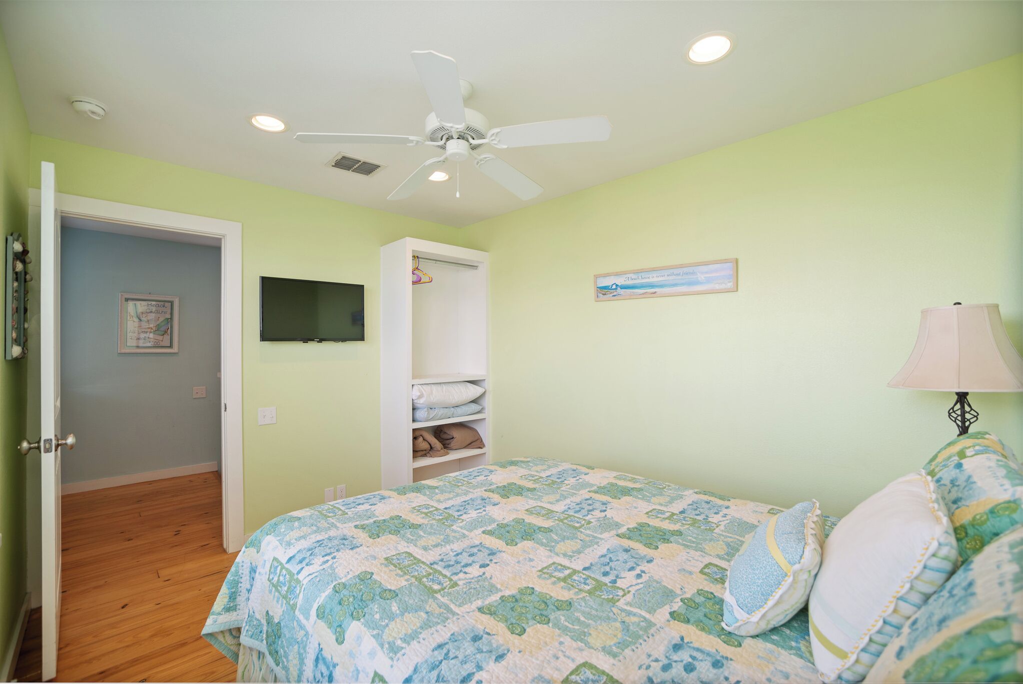 A bedroom with a bed, a ceiling fan, a TV, and a door leading to another room.