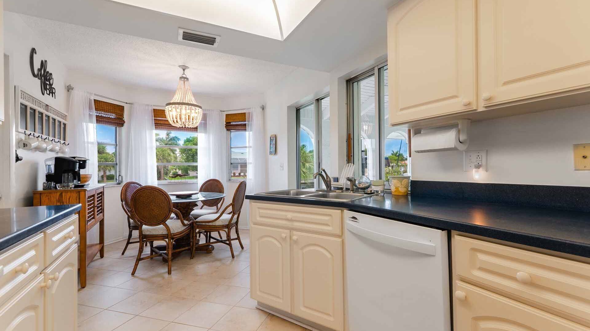 A modern kitchen with white cabinetry, a black countertop, and a dining area with wicker chairs.