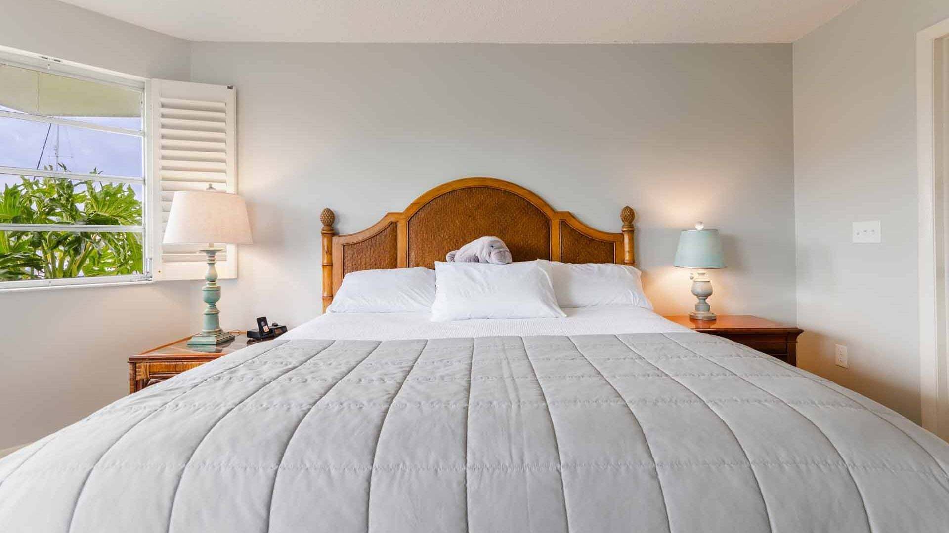 A neatly made bed with a wooden headboard, two bedside tables with lamps, and a window with blinds.