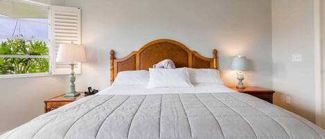 A neatly made bed with a wooden headboard, two bedside tables with lamps, and a window with blinds.