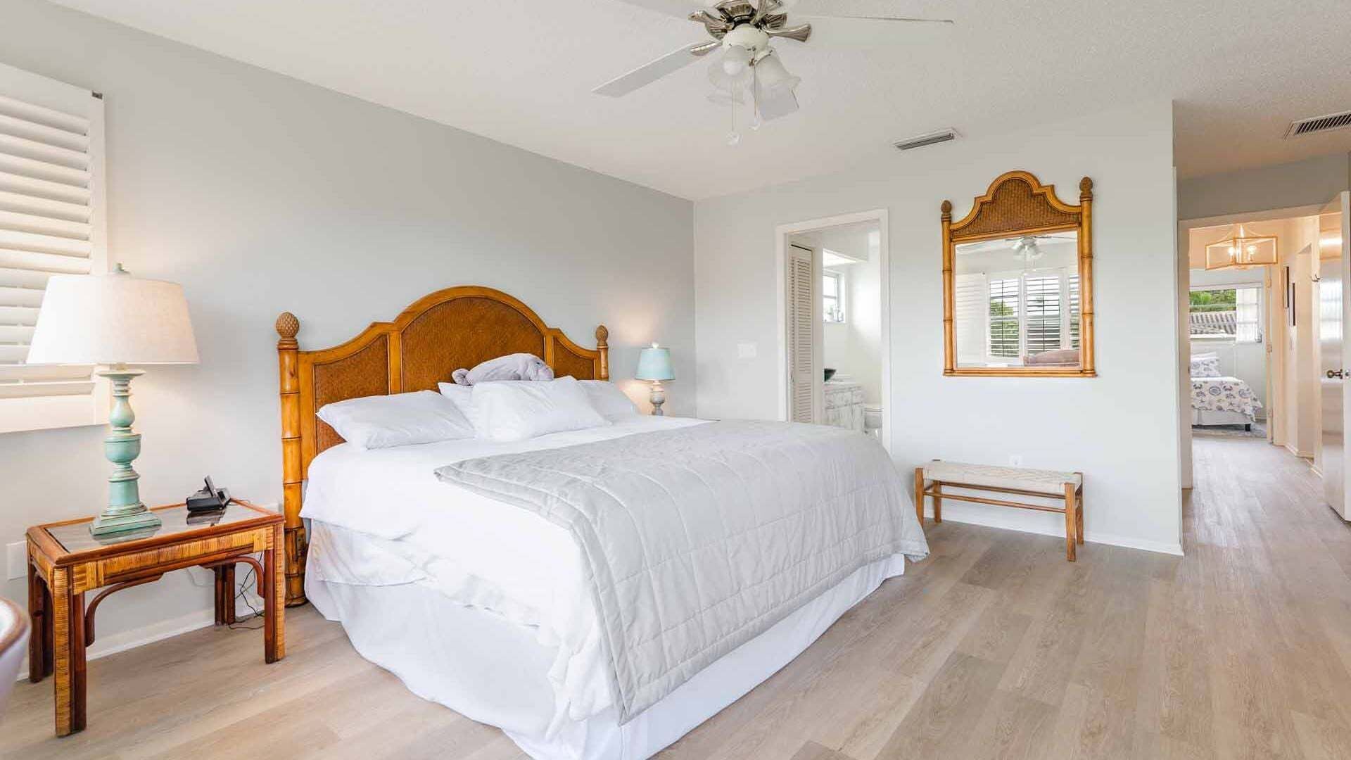 A bedroom with a wooden bed, a nightstand, a bench, a ceiling fan, and a mirror.