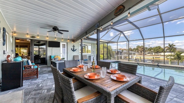 A covered outdoor area with a pool, dining table, chairs, and a ceiling fan. - Blc200 (Punta Gorda)