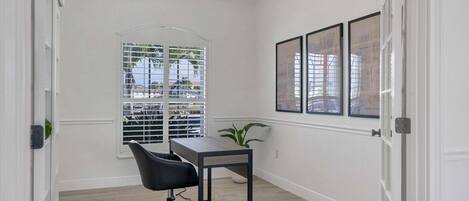 A room with a desk, chair, and a window with blinds.