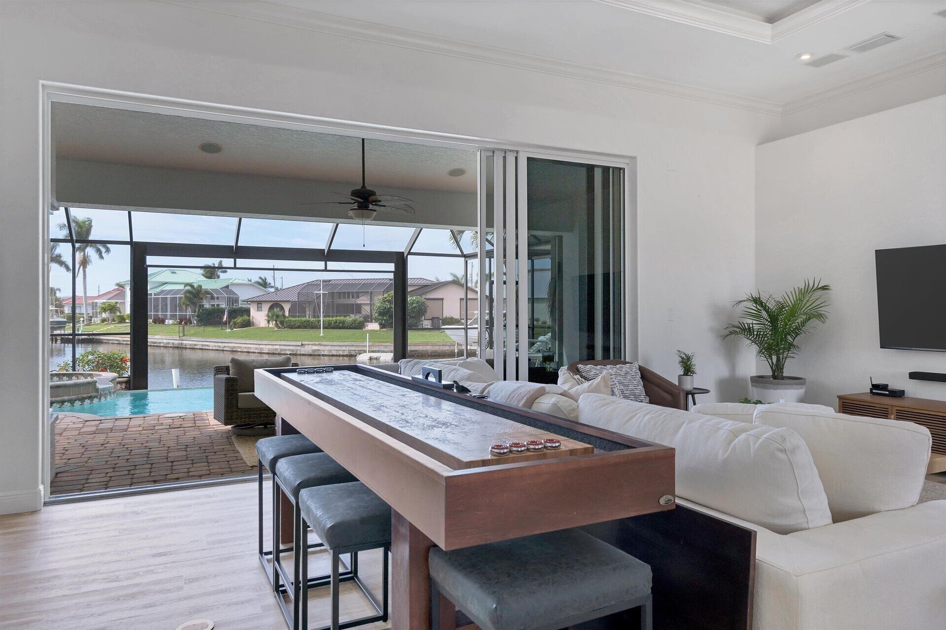 A modern living room with a pool table, comfortable seating, and a large sliding glass door leading to a pool area.