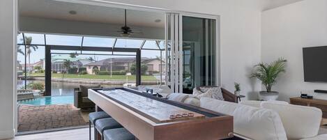 A modern living room with a pool table, comfortable seating, and a large sliding glass door leading to a pool area.