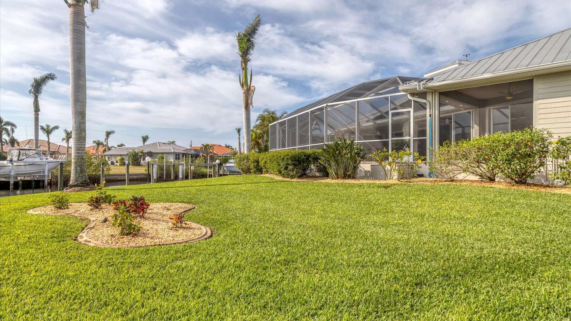 A well-maintained backyard with a greenhouse, palm trees, and a boat dock.