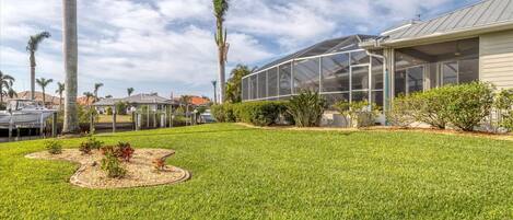 A well-maintained backyard with a greenhouse, palm trees, and a boat dock.
