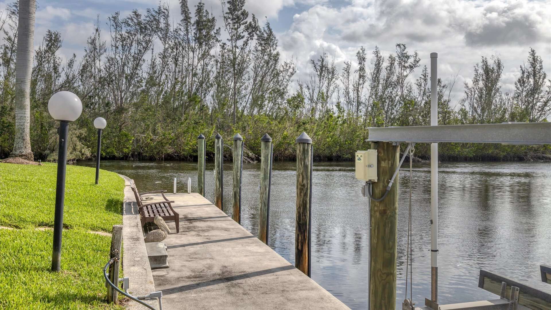 A concrete dock extending into a calm body of water, surrounded by lush greenery and tall trees.