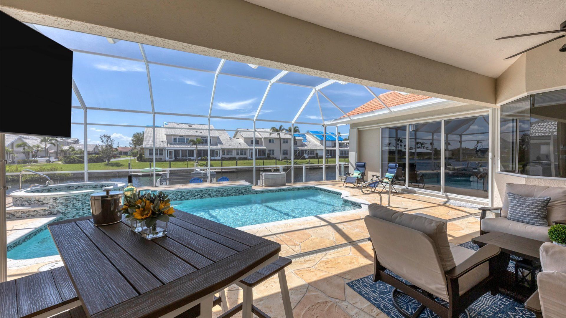 A covered outdoor area with a pool, seating, and a view of houses in the background.