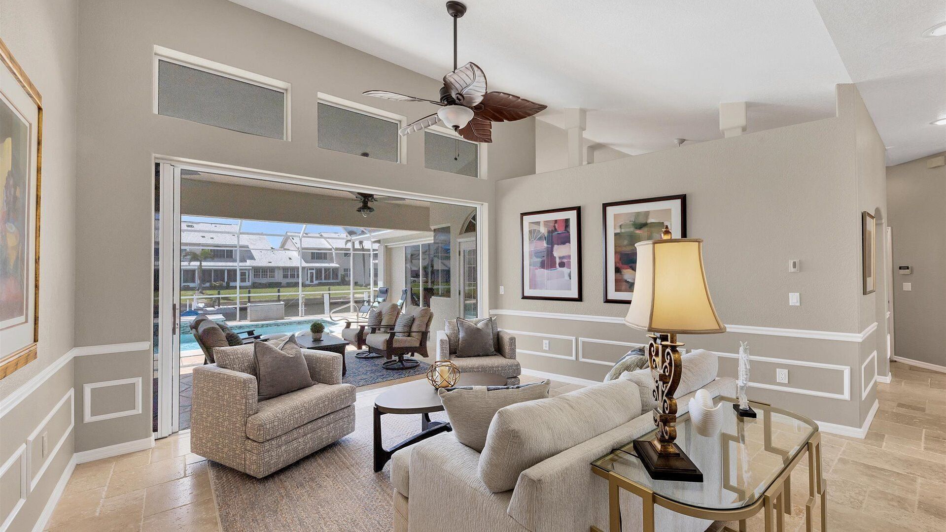 A spacious living room with a pool view, comfortable seating, and a ceiling fan.