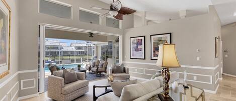 A spacious living room with a pool view, comfortable seating, and a ceiling fan.