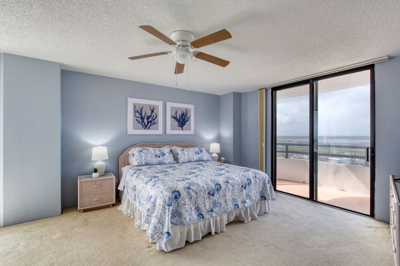 Ein Schlafzimmer mit einem Bett, zwei Nachttischlampen, einem Deckenventilator und einem großen Fenster mit Blick.