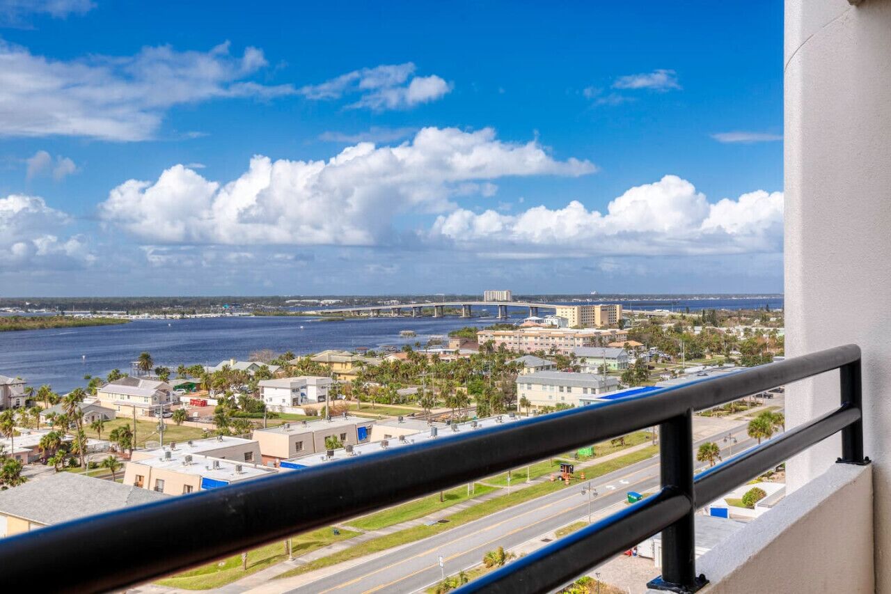 A view from a balcony overlooking a coastal cityscape with a bridge, buildings, and a clear sky.