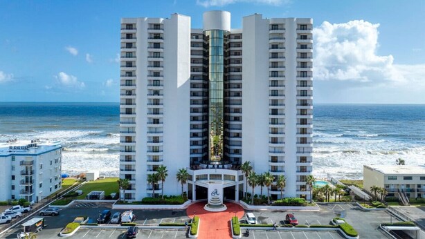 Un hotel di grandi dimensioni con un ascensore centrale in vetro, una strada a cerchio rosso e vista sull'oceano.