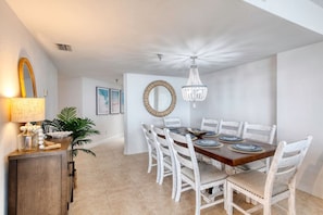 A dining area with a wooden table, white chairs, a chandelier, and a mirror on the wall.