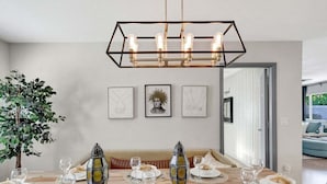 Un comedor con una mesa de madera dispuesta para una comida, una lámpara colgante y cuadros en la pared.