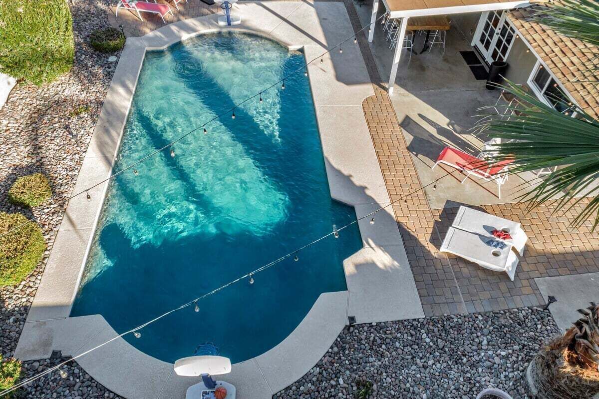A rectangular swimming pool with clear blue water, surrounded by a paved deck. There are lounge chairs and a small table near the pool.