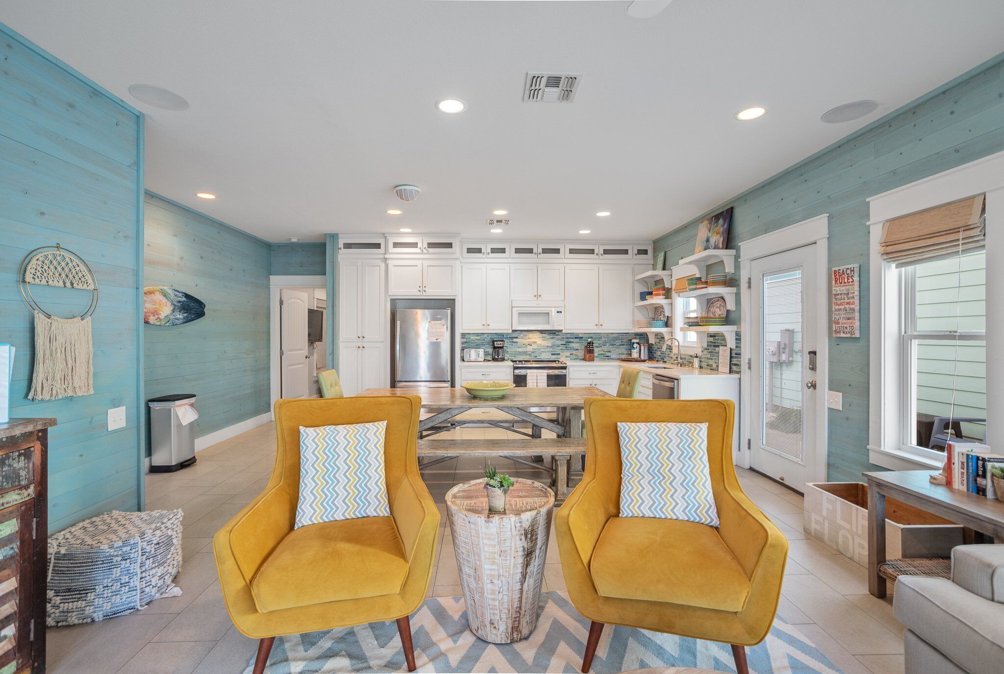 A spacious living room with two yellow armchairs, a central coffee table, and a kitchen in the background.