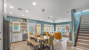 A spacious kitchen with a dining area, a staircase, and a living room with a sofa and chairs. - Pura Vida - Beach Gear Credit Included! (Port Aransas)