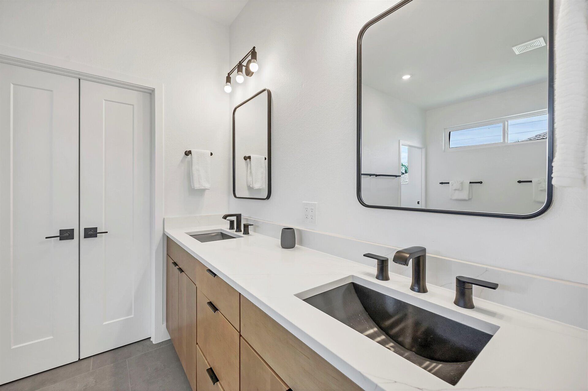 A modern bathroom with two sinks, a large mirror, and a vanity with drawers.