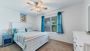 A bedroom with a white bed, a nightstand, a dresser, a ceiling fan, and a window with blue curtains. - Port Charlotte Private Waterfront Condo Wa4410-317 (Port Charlotte)