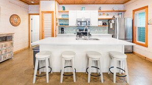 A kitchen with a large island, white bar stools, stainless steel appliances, and wooden ceiling. - Ruby Tuesday (Port Aransas)
