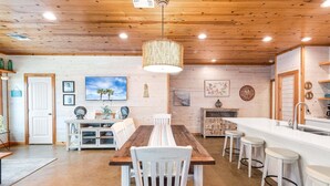 A wooden ceiling, a dining table with chairs, a kitchen area, and a bar with stools. - Ruby Tuesday (Port Aransas)
