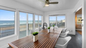 A modern room with a wooden table, white chairs, and potted plants. It features large windows with a view of the beach and ocean. - Pool, 7 Bedrooms, Direct Oceanfront, 4 Kitchens (Port Orange)