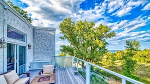A wooden deck with outdoor furniture, a stone wall, and a view of trees and landscape. - The Addition at Villa Santorini (Gary)