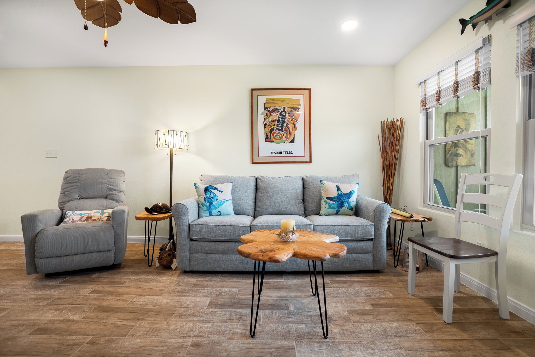 A living room with a grey sofa, a wooden coffee table, a grey armchair, a floor lamp, and a framed artwork on the wall.