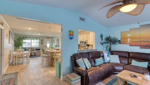 A living room with a brown leather sofa, a wooden coffee table, and a ceiling fan. - Under The Sea Pool and Hot Tub (Port Orange)