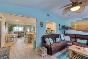 A living room with a brown leather sofa, a wooden coffee table, and a ceiling fan. - Under The Sea Pool and Hot Tub (Port Orange)