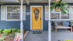 A house with a yellow front door, a porch with a bench, and a sign that reads "BEACH HOUSE". - Under The Sea Pool and Hot Tub (Port Orange)