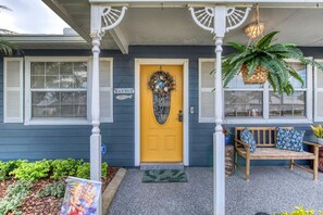 A house with a yellow front door, a porch with a bench, and a sign that reads 'BEACH HOUSE'. - Under The Sea Pool and Hot Tub (Port Orange)