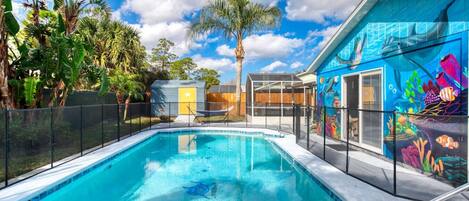 A swimming pool with a clear blue water, surrounded by a fence, and a colorful mural on the adjacent building.