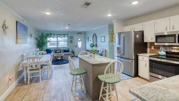 A modern kitchen with white cabinets, stainless steel appliances, and a central island with bar stools. - Under The Sea Pool and Hot Tub (Port Orange)