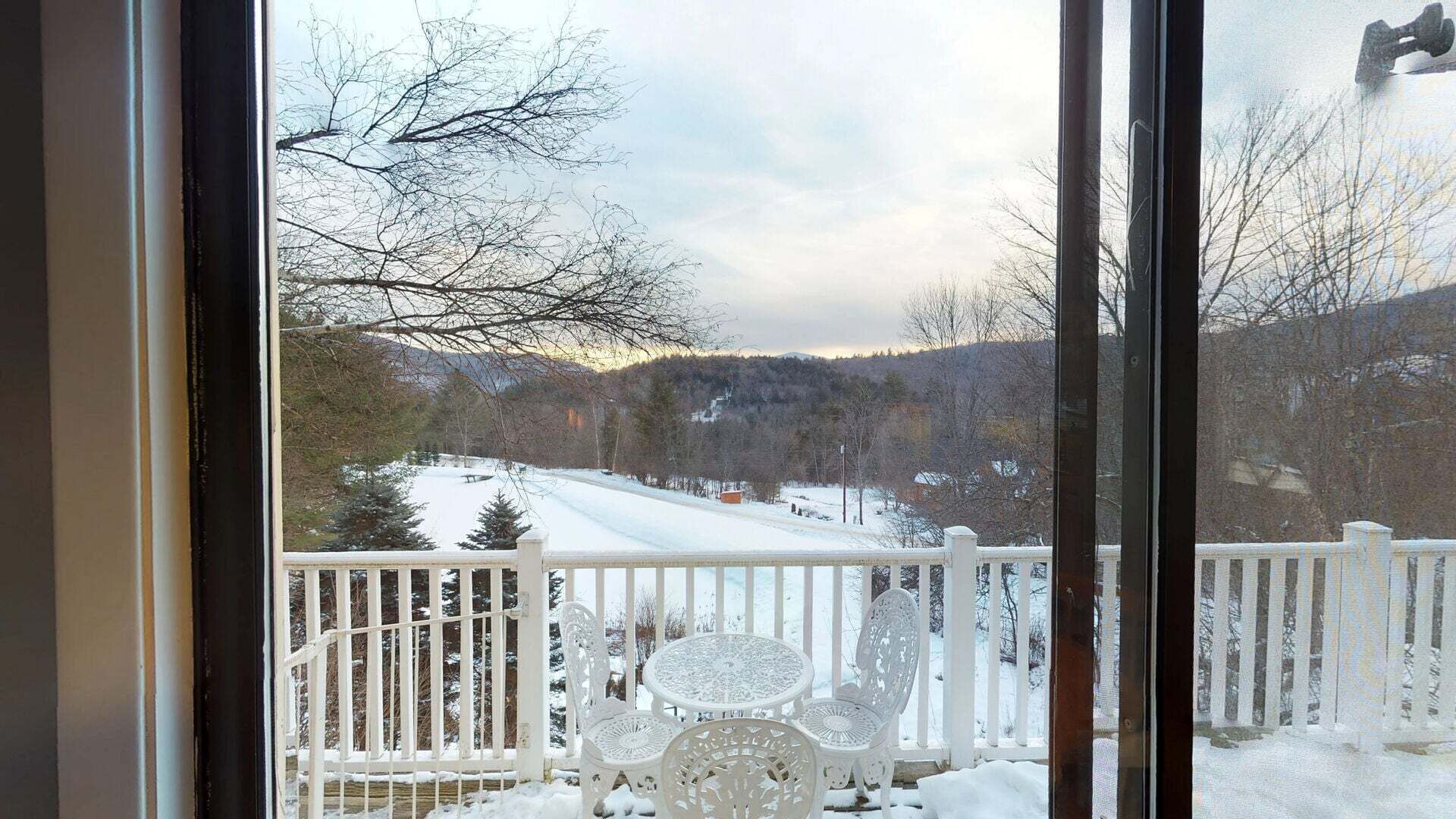 A view through a window with a white railing, snow-covered landscape, and trees.
