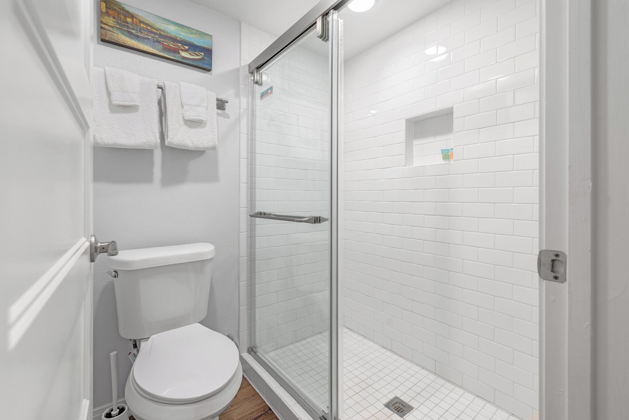 A modern bathroom with a glass-enclosed shower, white tiled walls, and a toilet.