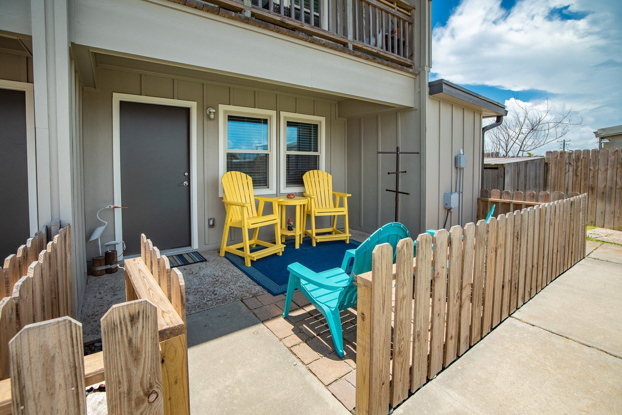 A two-story house with a front porch, a wooden fence, and outdoor seating with chairs.