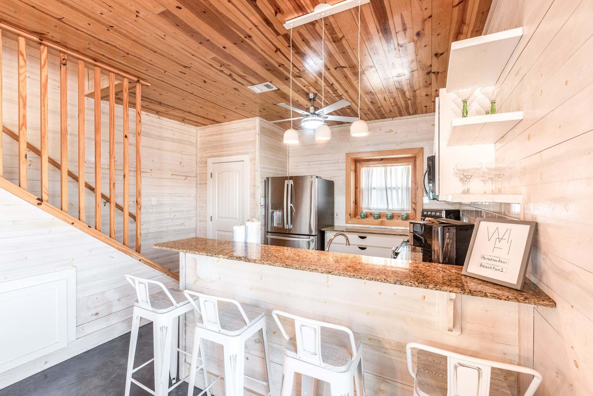 A kitchen with a central island, bar stools, a ceiling fan, and a refrigerator.