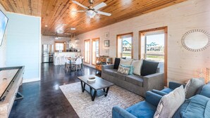 A spacious living area with a wooden ceiling, a sofa set, a coffee table, and a dining table. - Paradise Azul - Golf Cart & Shuffleboard! (Port Aransas)