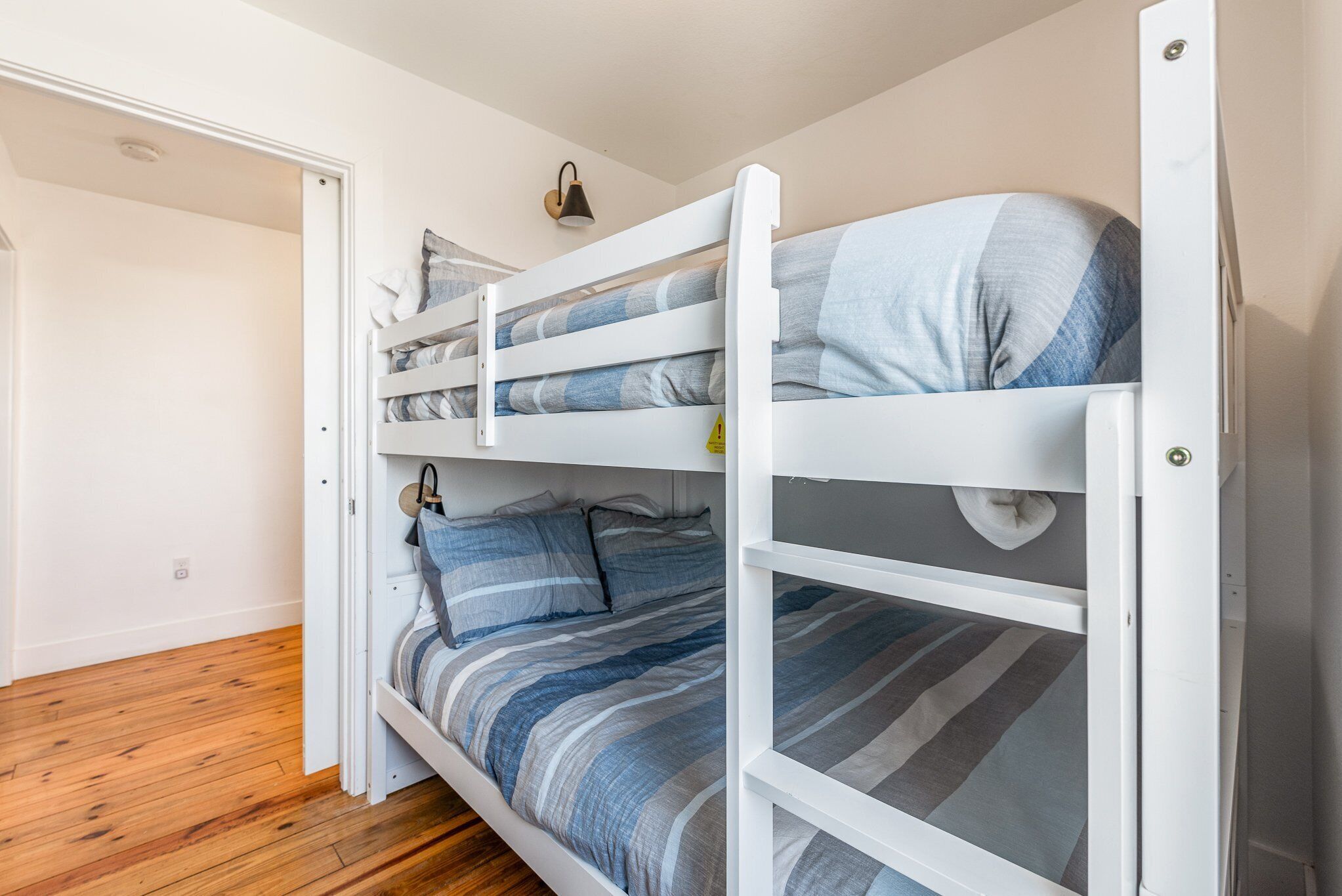 Ein Stockbett mit gestreifter Bettwäsche in einem Zimmer mit Holzboden und weißen Wänden.