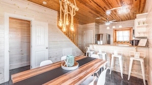 A wooden interior with a dining area, white chairs, a wooden table, and a kitchen with white bar stools. - Paradise Azul - Golf Cart & Shuffleboard! (Port Aransas)