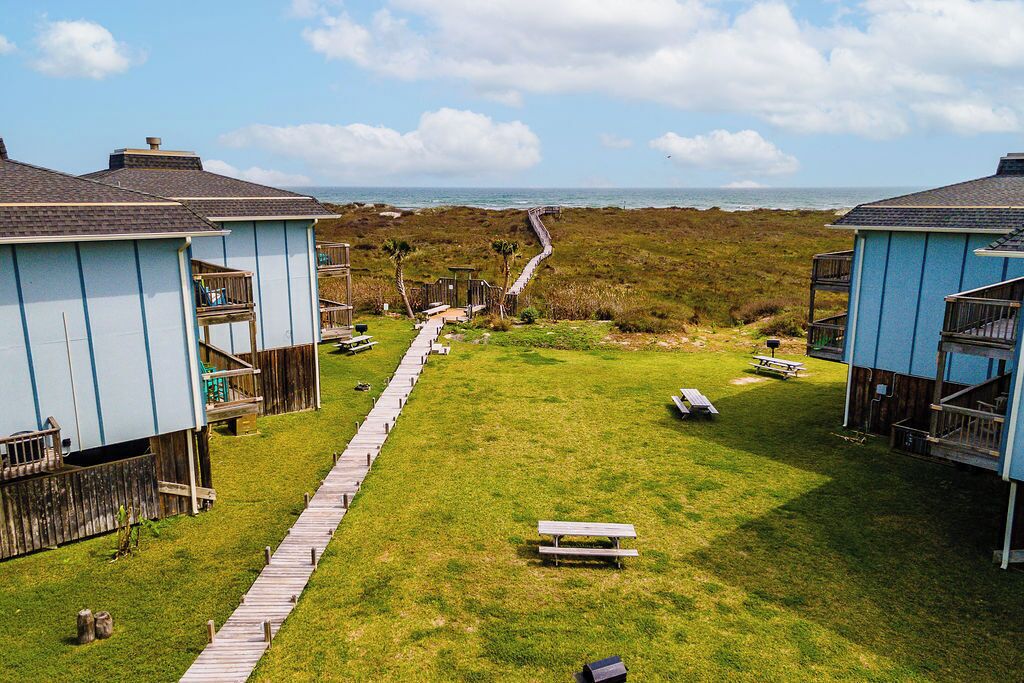 Ein Küstenanwesen mit Rasengrundstück, Holzterrasse und Zugang zum Strand.