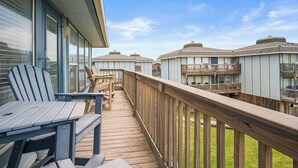 A wooden deck with Adirondack chairs and a table, overlooking a residential area with multiple buildings.