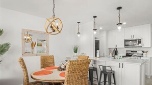 A modern kitchen with white cabinets, a central island, and a dining area with wicker chairs and a round table.