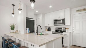 A modern kitchen with white cabinets, a large island with bar stools, stainless steel appliances, and pendant lighting.