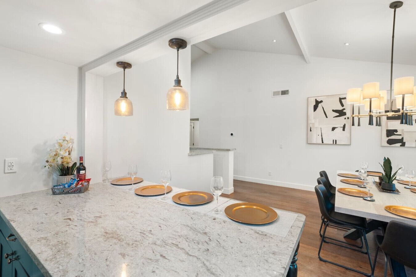 A modern kitchen with a marble island, pendant lighting, and a dining area with a white table set for six.