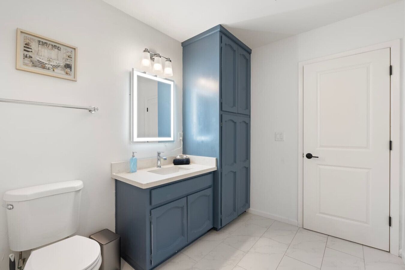 A bathroom with a white toilet, a white sink with a mirror, and a blue cabinet.